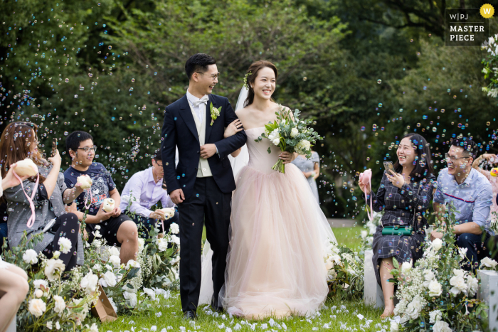 La novia y el novio salen de su ceremonia al aire libre con invitados soplando burbujas