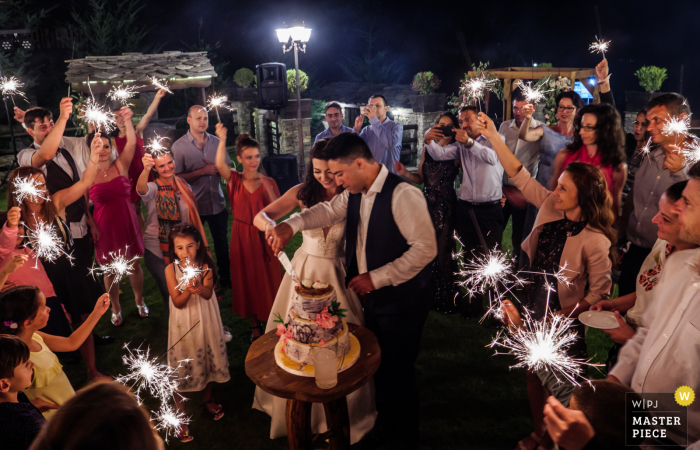 A noiva e o noivo, rodeados pelos convidados do casamento, cortam o bolo na Residência Glavatarksy Han na Bulgária