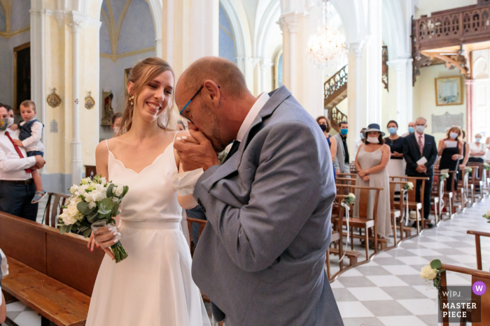 Kościół w Poussan France ślubny wizerunek taty panny młodej całujący ją w rękę po prowadzeniu jej do ołtarza