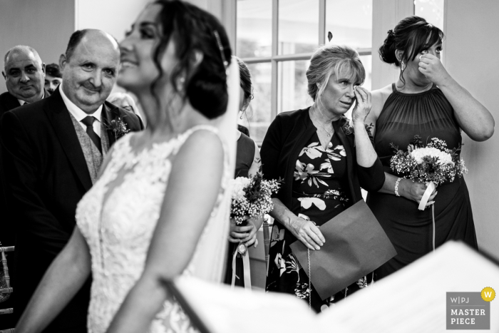 Black and white image of the Mother of the bride and bridesmaid wiping away tears during ceremony at Iscoyd Park in the UK