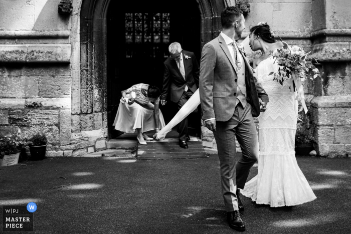 The veil catches as the bride and groom leave the St Mary Magdalene Church in Brampton, UK The veil catches as the bride and groom leave the St Mary Magdalene Church in Brampton, UK