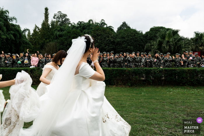 Los recién casados ​​de China han terminado la ceremonia de la boda. Están listos para salir de la ceremonia. Hay muchos estudiantes de entrenamiento militar alrededor de la ceremonia. También celebran la boda de la novia. Esto es inesperado. Saludan felices a la novia.