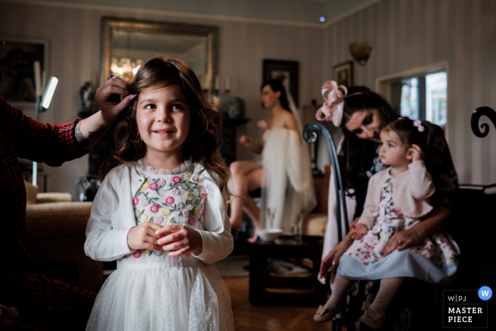 Una de las niñas de las flores de la pareja sonríe se ha arreglado el cabello, mientras su hermana pequeña se sienta en la rodilla de su madre, con la novia al fondo en Larne, Irlanda del Norte.