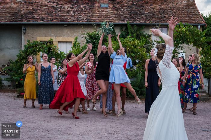 French brides throws her bouquet to the very eager single ladies who stretch out to catch it.