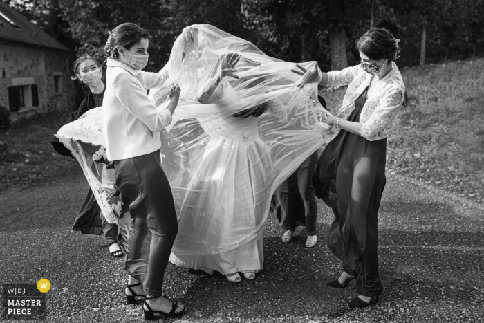 Huwelijksfotografie uit Frankrijk Serans van de bruid die hulp krijgt met haar jurk op weg naar de ceremonie