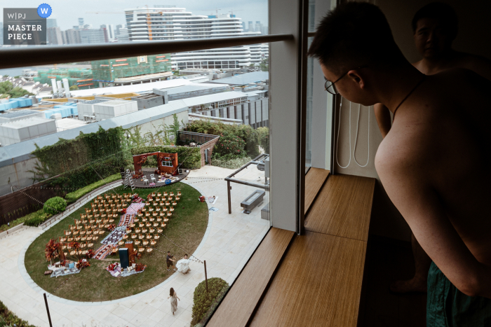 Hochzeitsfoto aus Quanzhou Fujian, auf dem der Bräutigam von seinem Hotelzimmer aus einen Blick auf den Ort der Zeremonie wirft