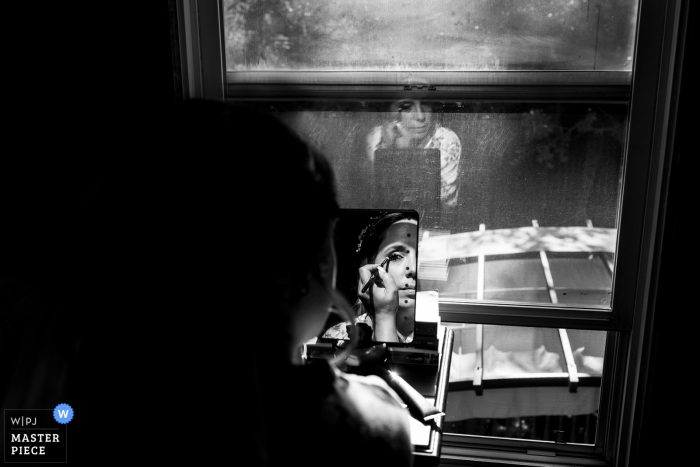 Canadian bride applies her makeup in window light