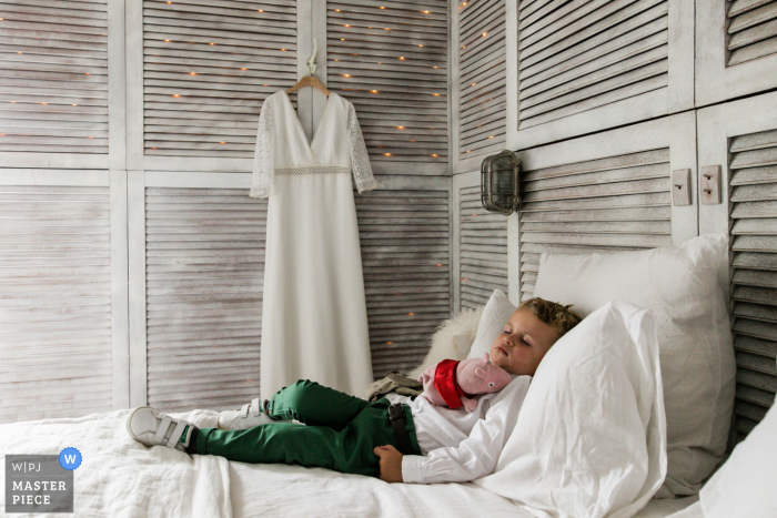 Fotografia di matrimonio in Francia di un bambino che schiaccia un pisolino accanto all'abito appeso alle spose