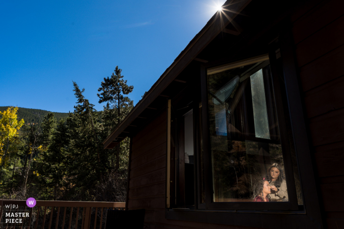 Kleine Hochzeitsfotografie von einem Privathaus in Colorado, auf der sich die Braut in einem beleuchteten Fensterrahmen vorbereitet