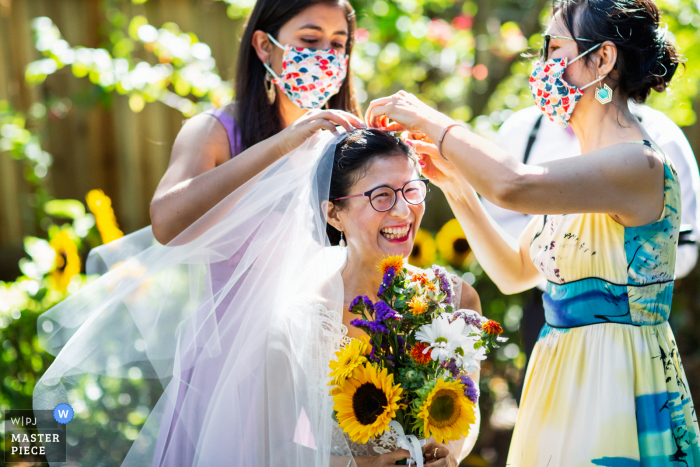 Brautjungfern, die den Schleier noch einmal auf der glücklichen Braut bei ihrer Hochzeit in Oakland, CA, anpassen