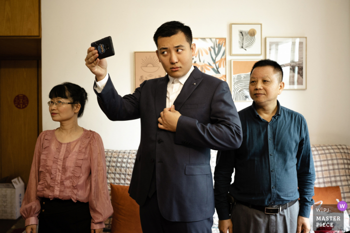 Huwelijksfoto in Guangdong van de bruidegom die zichzelf controleert om er zeker van te zijn dat alles perfect is voor de ceremonie, met zijn ouders aan elke kant van hem