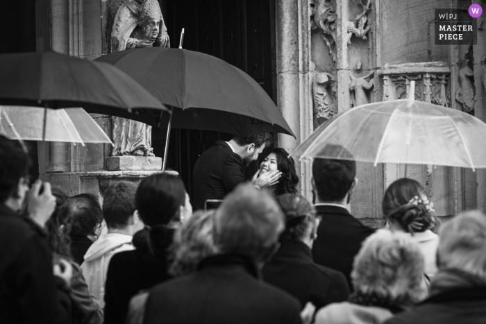 Il fotografo di matrimoni francese ha realizzato questa immagine in Serans della sposa e dello sposo circondati da ospiti con ombrelli