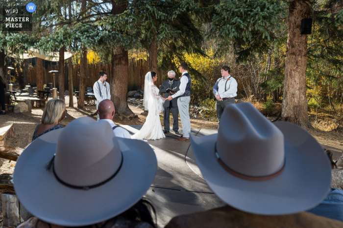 Imagen de boda de Colorado tomada a través de sombreros de vaquero en la ceremonia en esta ceremonia al aire libre