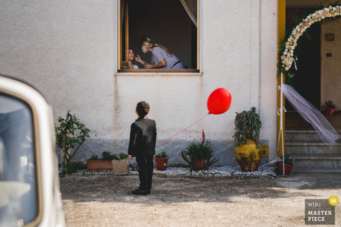 Photo by: <a href="https://www.wpja.com/contests/2020-v04/best-wedding-photographers/2602371">Marco Colonna - Palagiano Taranto</a> Italian wedding photo of a young child with a red balloon watching the bride have her makeup done