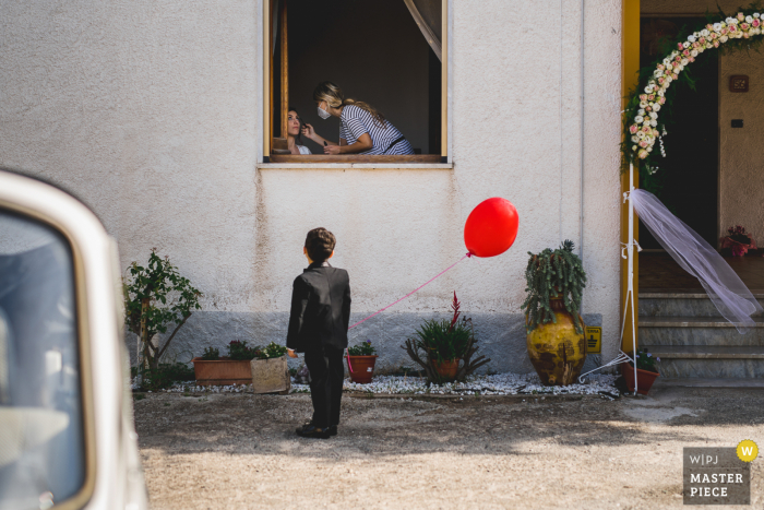 Italiaanse trouwfoto van een jong kind met een rode ballon die kijkt naar de make-up van de bruid - IT-film