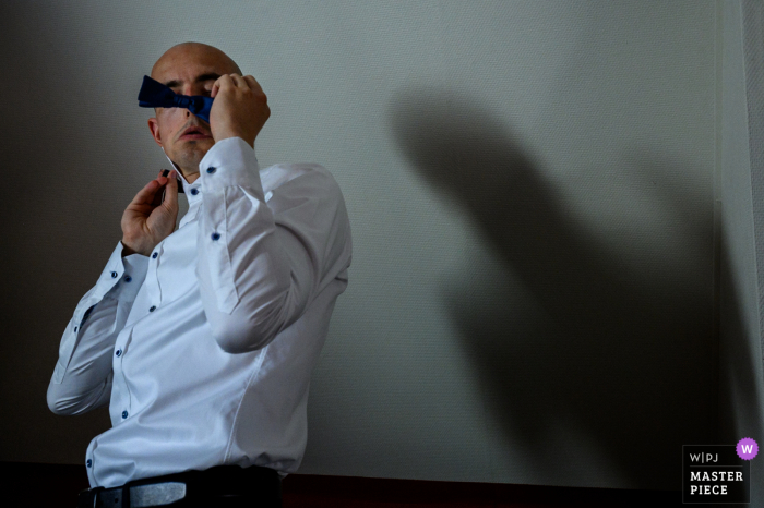 Photo by: <a href="https://www.wpja.com/contests/2020-v04/best-wedding-photographers/2602542">Sven Soetens - Stekene </a> Belgium groom is putting on his tie with his shadow cast behind him on the wall