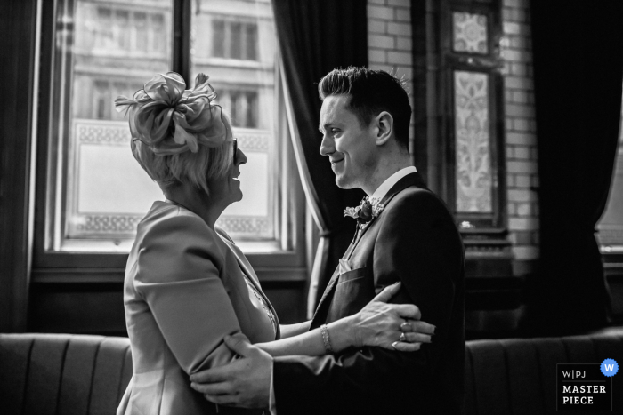 Huwelijksfoto in het Verenigd Koninkrijk van de bruidegom met zijn moeder die elkaar omhelzen in het stadhuis van Manchester