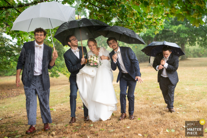 Cromac trouwfoto van de bruid, bruidegom en groomsmen die met paraplu's lopen terwijl de regen naar beneden komt