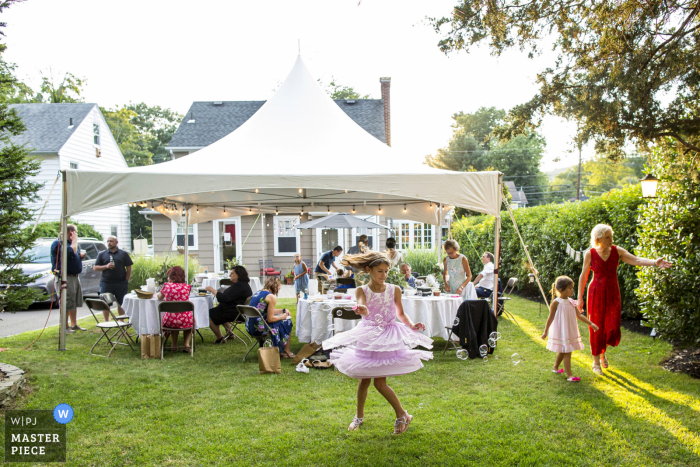 Fotografia di matrimonio nel New Jersey da un ricevimento in giardino di una bambina che gira in bolle mentre il sole tramonta durante un matrimonio intimo nel cortile