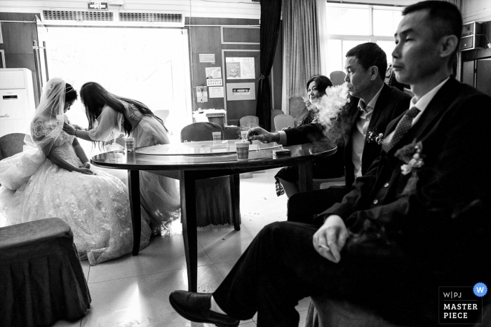 Fotografía de la boda de Chengdu de Sichuan de La novia y sus padres están esperando que comience la ceremonia. A la izquierda, la hermana de la novia arregla su vestido de novia. A la derecha, el padre de la novia escupe humo. En el lejano