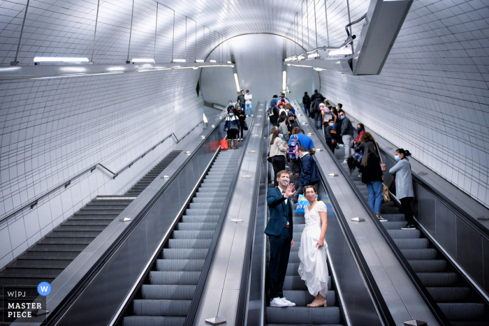 Huwelijksfotografie vanuit de metro van Toulouse tijdens de uitgang van de metro op de roltrap terwijl de bruidegom zijn hand naar zijn gasten zwaait