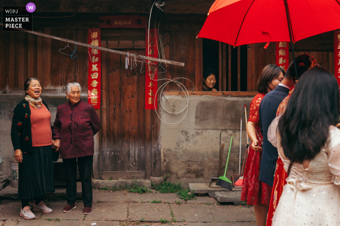 A Fujian wedding photographer captured onlookers watching as the bride and groom pass in the streets under a red umbrella