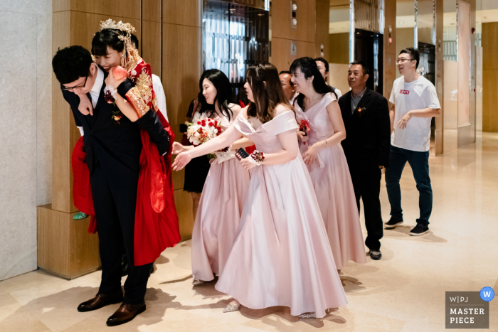 Um fotógrafo de casamento de Pequim nos mostra uma imagem do noivo carregando a noiva para levá-la ao carro do casamento - Como as roupas estão muito escorregadias, a noiva está prestes a cair. As damas de honra se apressam para ajudar o noivo a segurar a noiva