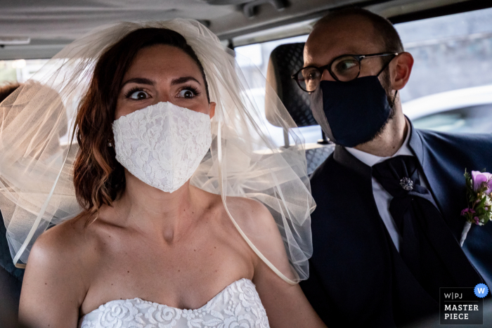 Huwelijksfotografie vanuit de auto in het Grand Hotel Baia Verde - Aci Castello toont de specifieke uitdrukking van de bruid, die bij het masker moet blijven terwijl ze met de bruidegom beweegt