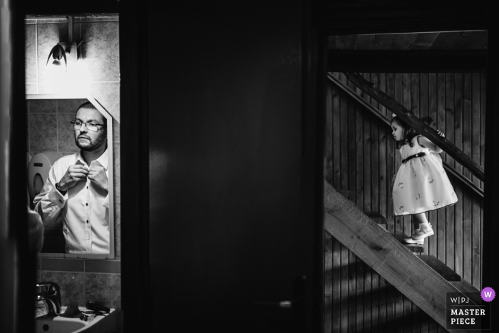 Photo by: <a href="https://www.wpja.com/contests/2020-v04/best-wedding-photographers/2604645">Daniel Monteiro - Porto </a> Zagreb, Croatia wedding photography of the groom fixing his shirt and tie as a girl plays on the stairs