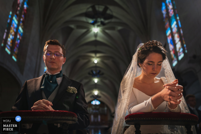 A Brittany wedding photographer captured this prayer moment at Brissac-Quincé, France of the Bride and groom during the ceremony