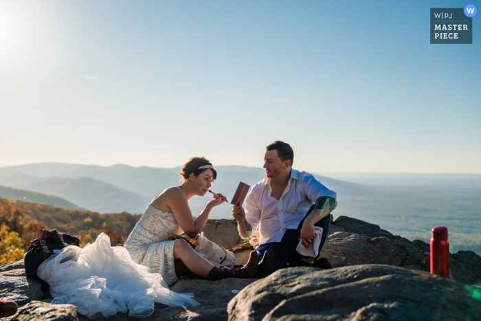 Il fotografo di matrimoni della Pennsylvania ha creato questa immagine di una cerimonia dello sposo di Filadelfia che aiuta la sua sposa a ritoccare il trucco dopo l'escursione fino alla cima di questa montagna per la loro cerimonia di fuga