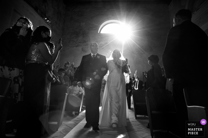 Der Hochzeitsfotograf von Reggio Calabria schuf dieses Bild in der alten Kirche von Carafa Castle in Roccella Jonica, Italien, das den Eintritt der Braut in die Kirche zeigt