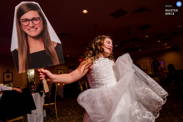 Imagen del lugar de la boda de Belmont Country Club de la niña de las flores bailando con un recorte de un miembro de la familia que no puede asistir a la fiesta de recepción de la boda