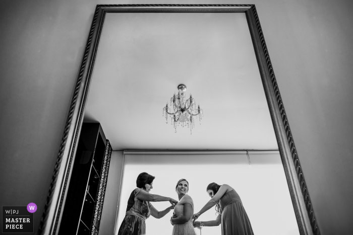 Rio Grande do Sul wedding photographer created this image at Mirage - Porto Alegre of the Bride putting the dress together with her mother and sister 