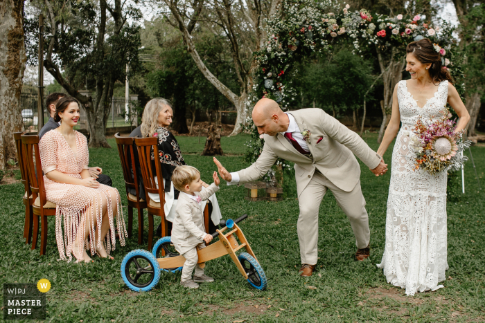 Fotógrafo de bodas de Rio Grande do Sul tomando fotografías en una ceremonia en el patio trasero de la casa del novio saludando a su hijo