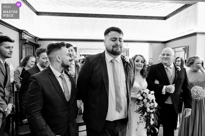 Il fotografo di reportage di matrimonio in Inghilterra ha catturato questa immagine in bianco e nero a Pendrell Hall che mostra lo sposo sopraffatto dall'emozione durante l'ingresso della sposa