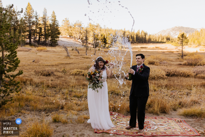 Fotografía de boda después de una ceremonia al aire libre en New Washoe City, NV de La novia y el novio sorprendidos por la explosión de champán debido al cambio de altitud