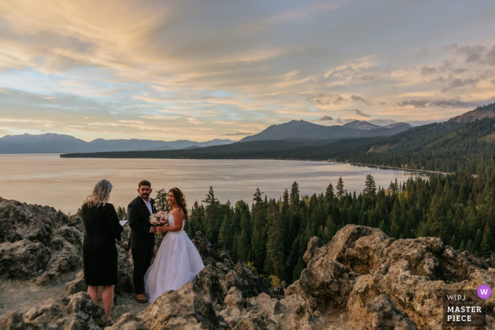 Fotografia remota de casamento ao ar livre na Califórnia em Tahoe City, Califórnia, mostrando o casal de noivos ouvindo seu oficiante em sua cerimônia do nascer do sol