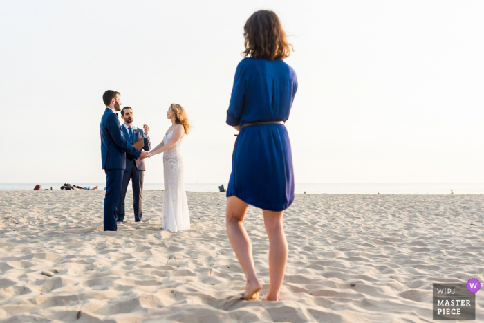 Strandhuwelijksfotografie in Californië uit Cupertino, CA met een gast die toekijkt als een bruid en bruidegom trouwen in een intieme strandceremonie