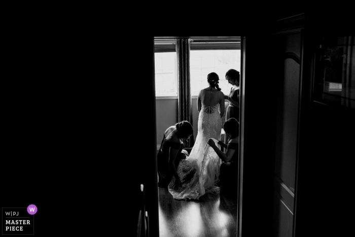 Foto de boda de Alberta desde el hogar de la novia vista a través de la puerta vistiéndose con damas de honor