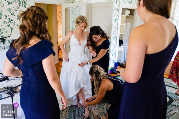 Bridesmaids help the bride put on her shoes at her Northeast Harbor Maine wedding in this real moment photo