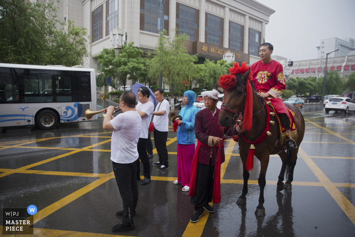 Foto di un fotografo di matrimoni dello Shaanxi di uno sposo a cavallo per le strade durante la pioggia