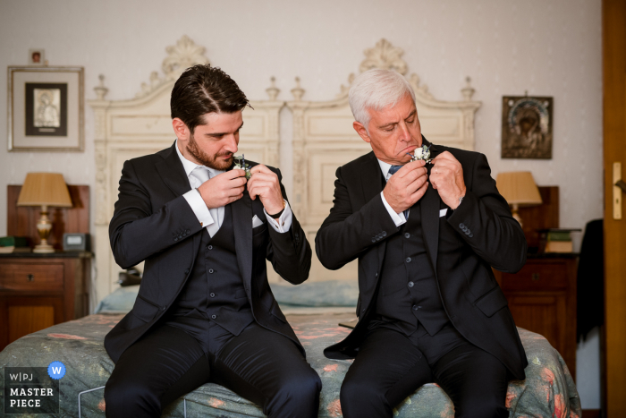 Foto de boda de Taranto de Apulia en la casa del novio mientras el novio y el padre ajustan el ojal de su chaqueta