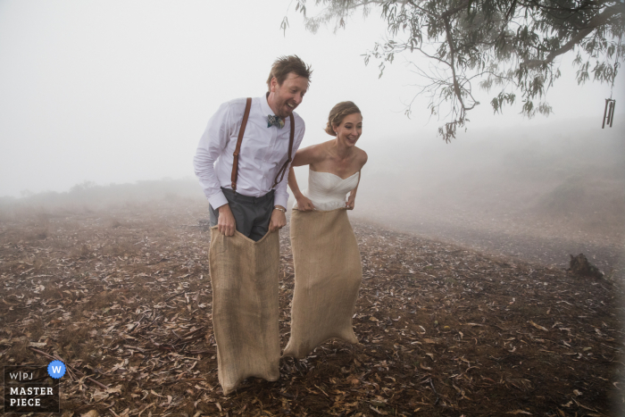 Wedding photography overlooking the pacific ocean near Stinson Beach, California of the bride and groom in a potato sack race