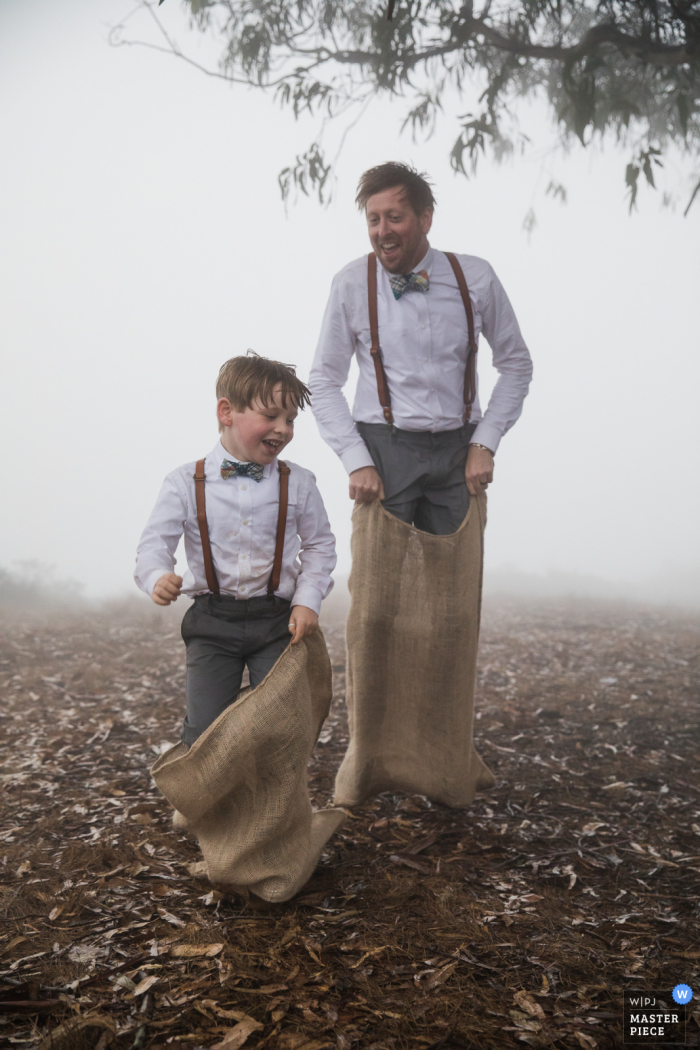 Wedding photo from the cliff edge overlooking the pacific ocean near Stinson Beach, California of a really close potato sack race -- a time honored tradition