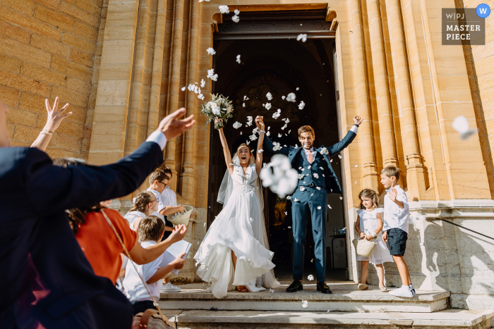 Imagen de boda Auvergne-Rhône-Alpes que muestra la salida de la iglesia de los novios con spray de pétalos