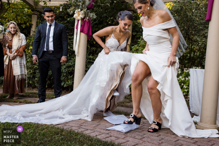 The North House, Avon CT wedding image of brides lifting their dresses and triumphantly smash their respective glasses during the breaking of the glass at their jewish wedding ceremony