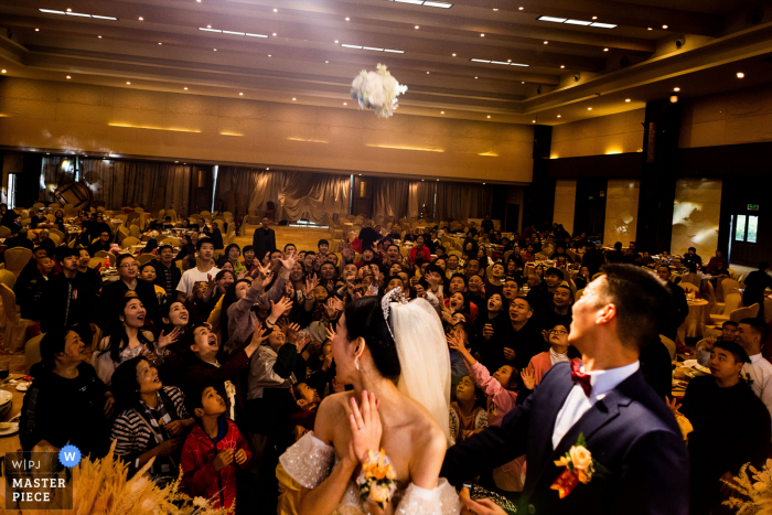 Fotografía de la boda del lugar de Sichuan de La novia arrojando la flor en su mano, que es un símbolo de amor y felicidad, detrás de ella. Los amigos de los recién casados ​​están arrebatando flores y muchas manos se estiran