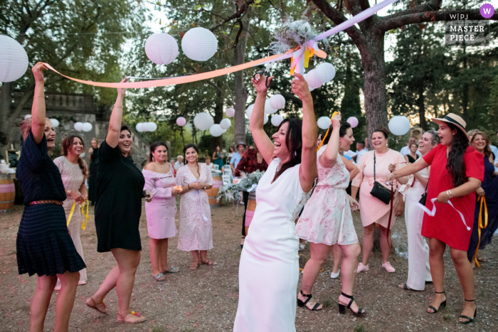 Fotografia de casamento ao ar livre na França no parque da vila de Claret mostrando muita atmosfera durante o jogo da fita para o buquê de noiva