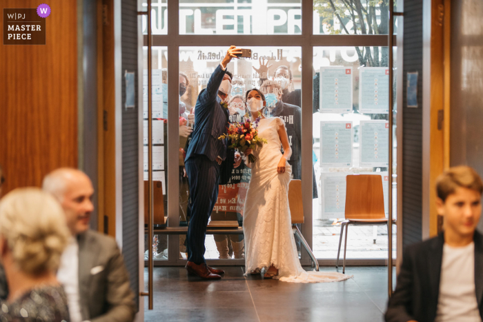 Foto di matrimonio dalle Fiandre: gli sposi si scattano un selfie con amici isolati fuori dal municipio subito prima della cerimonia